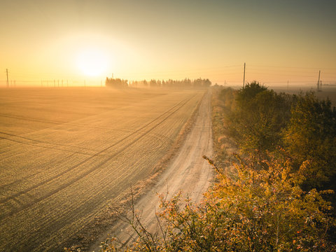 Dirt road leading towards sunrise - agriculture themed. Autumn golden hour.