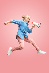 Beautiful young child teen girl jumping with megaphone isolated over pink background. Runnin girl...