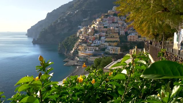 Positano, Amalfi Coast, Salerno, Italy at spring time. Crane shot of Positano village at sunset lights, yellow flowers on foreground. UHD, 4K