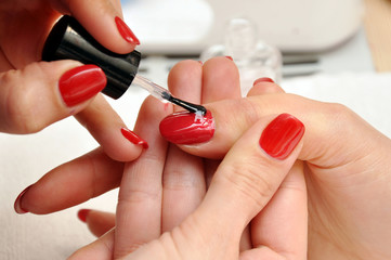A manicurist paints a customer's nails. Painting nails with red lacquer close-up.