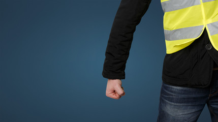 Yellow vests protests. Unrecognizable man clenched his fist in protest on blue background....