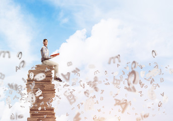 Man student on stack reading book and symbols flying around