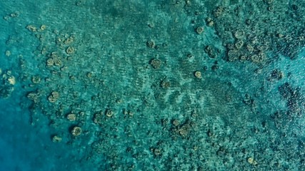 stunning aerial drone image of a a small fishing boat entering an a sea ocean anchorage in a channel next to a coral reef in crystal clear azure blue water at a remote isolated tropical island