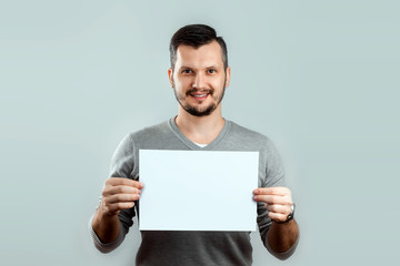 A young, attractive man holding a blank white A4 sheet, on a light background. mockup, layout, copy...