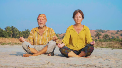 Senior couple sits and meditating together on sandy beach