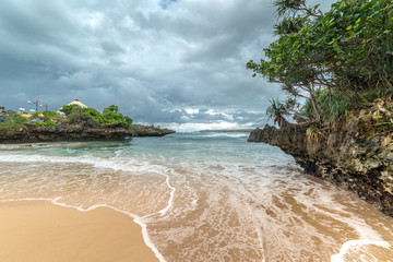 Sandy beach with rocky mountains and clear water of Indian ocean at cloudy day. Bali, Indonesia