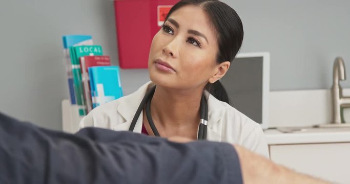 Close up on Japanese woman primary doctor listening to patient on exam table