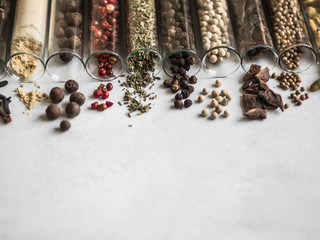Various dry spices in glass tubes and spilled on gray background. Copy space.