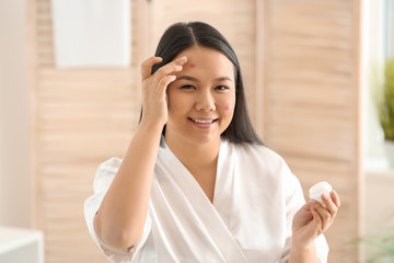 Portrait of young Asian woman with acne problem applying cream in bathroom