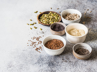 Various seeds - sesames, flax seed, sunflower seeds, pumpkin seed, poppy, chia in bowls on a gray background. Copy space.