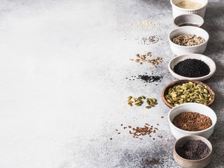 Various seeds - sesames, flax seed, sunflower seeds, pumpkin seed, poppy, chia in bowls on a gray background. Copy space.