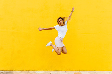 Fototapeta na wymiar Happy girl jumping on a yellow background