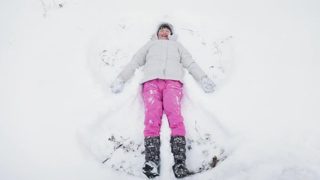 Happy kid girl making snow angel lying on the snow, winter children fun in slow motion