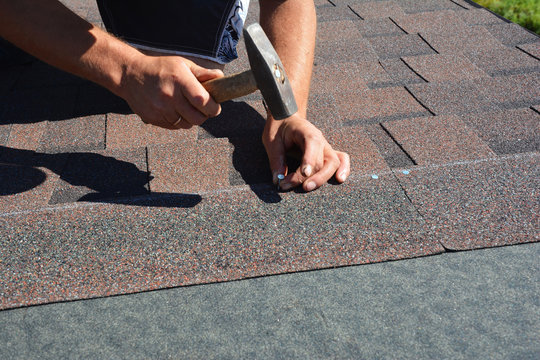 Roofing Construction. Roofer installing asphalt shingles on house construction roof corner with hammer and nails.