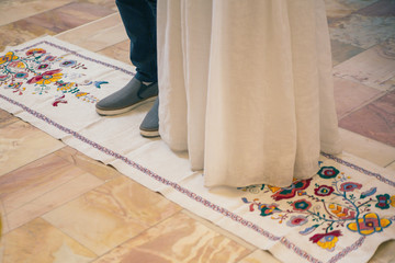 Fototapeta na wymiar The legs of the bride and groom become on embroidered towel, traditionally at a wedding ceremony in the church. Appear from the bottom to the legs.