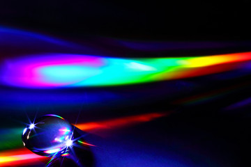 Water droplet on a compact disc refracting colourful light beams