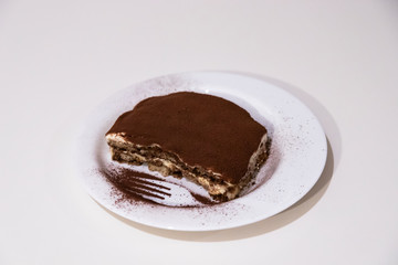 Homemade tiramisu, in a white ceramic plate, isolated on white background. Traditional Italian dessert, with cocoa, coffee, mascarpone and biscuits.