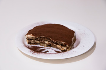 Homemade tiramisu, in a white ceramic plate, isolated on white background. Traditional Italian dessert, with cocoa, coffee, mascarpone and biscuits.