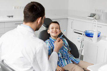 medicine, dentistry and healthcare concept - male dentist giving toothbrush to kid patient at dental clinic