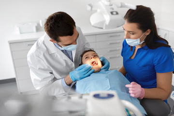 Naklejka na ściany i meble medicine, dentistry and healthcare concept - dentist with mouth mirror checking for kid patient teeth at dental clinic