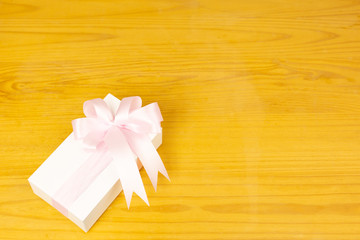 Gift box with pink ribbon on wooden background.