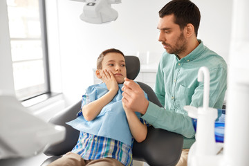 medicine, dentistry and healthcare concept - father supporting son suffering from toothache at dental clinic