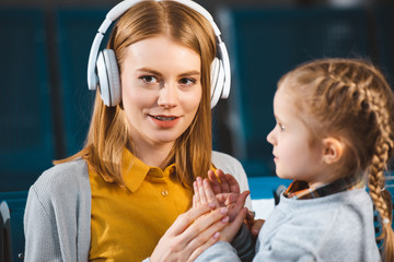 selective focus of attractive mother listening music in headphones near daughter