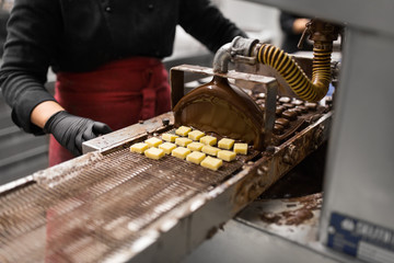 production, candy shop and people concept - confectioner making candies by chocolate coating machine at confectionery