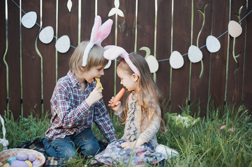 Naklejka premium Little girl and boy eat a gingerbread cookie in the shape of the Easter egg.