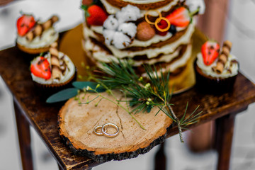 Wedding cake with fruit and an old wooden table with decorations and rings during a wedding ceremony in winter on snow in the middle of a forest covered with fresh snow