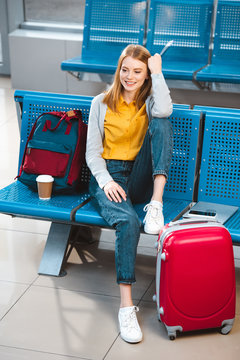 attractive woman sitting in waiting hall of airport near backpack and baggage