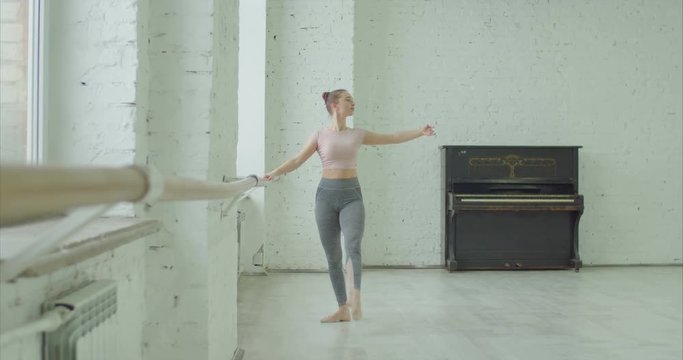 Graceful classic ballet dancer practicing tombee exercise at barre during rehearsal in ballet studio. Ballerina performing different choreographic exercises and dance moves in dance studio.