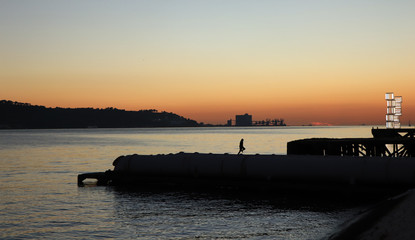 Fototapeta na wymiar Man walking in a jetty with a river in background at the sunset. Lisbon Portugal