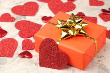 Red hearts and gift box closeup on a light concrete background. Valentine's Day.