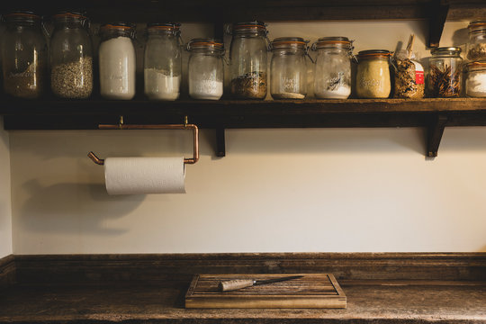 Wooden chopping board and knife on vintage wooden kitchen cupboard, row of glass jars with cooking ingredients on a wooden shelf.