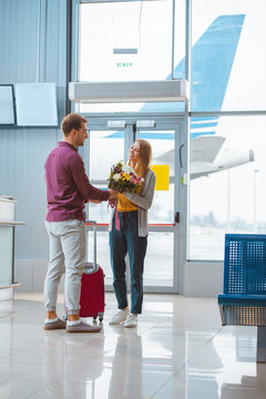 Cheerful Boyfriend Giving Flowers To Girlfriend In Airport