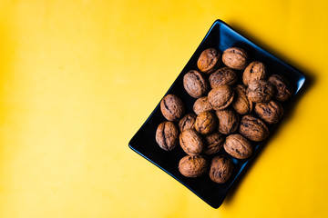 Black plain dish full of nuts on a yellow background.