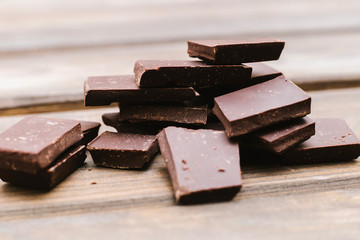Dark chocolate is lying on a wooden background. Soft focus