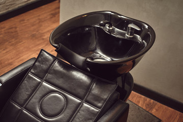 Black leather seat with wash basin in a barbershop interior with towels and shampoo on the side.