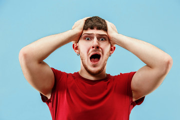 Screaming, hate, rage. Crying emotional angry man screaming on blue studio background. Emotional, young face. male half-length portrait. Human emotions, facial expression concept. Trendy colors