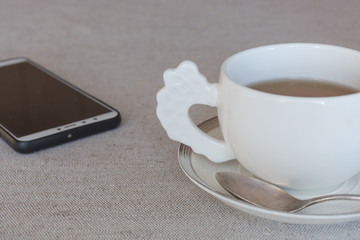Coffee break at work - White tea cup with plate and smartphone on linen table background