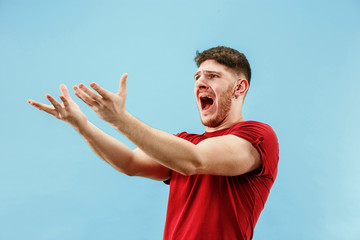 Screaming, hate, rage. Crying emotional angry man screaming on blue studio background. Emotional,...
