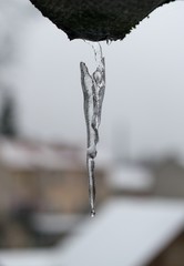 Icicle and falling drop against a gray sky