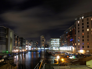 Fototapeta na wymiar Clarence dock leeds at night with moored barges and moonlit clouds over brightly illuminated waterside buildings reflected in the harbour