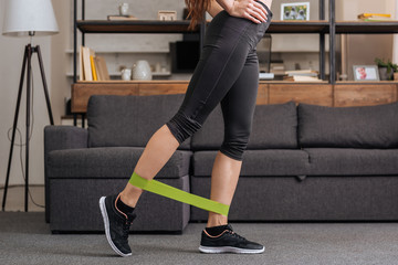 low section of sportswoman training with resistance band at home in living room