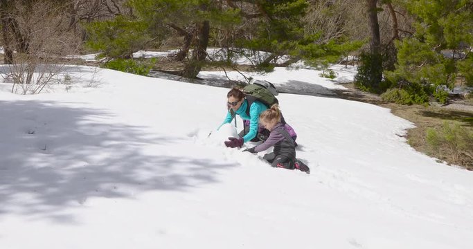 Happy family. Four years old blonde child and woman mother, sitting on knees playing touching snow to make a snowman in winter mountain. 4k video. 