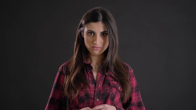 Portrait of caucasian long-haired brunette girl discontentedly watching into camera on black background.