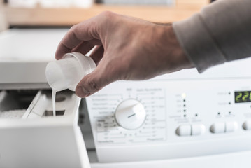 close-up of person using dosing aid to fill fabric softener into washing machine
