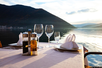 restaurant table with glasses napkins devices against the sunset of the sea of mountains and sky