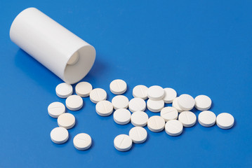 White tablets and bottle for tablets on blue background